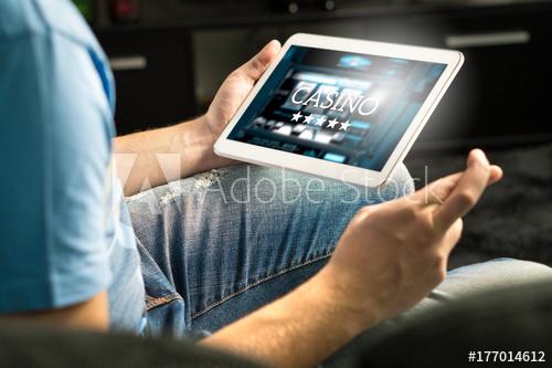 Excited man playing in an online casino with tablet fingers crossed wishing and hoping to win. Slot machine app. Person holding smart mobile device in hand at home.